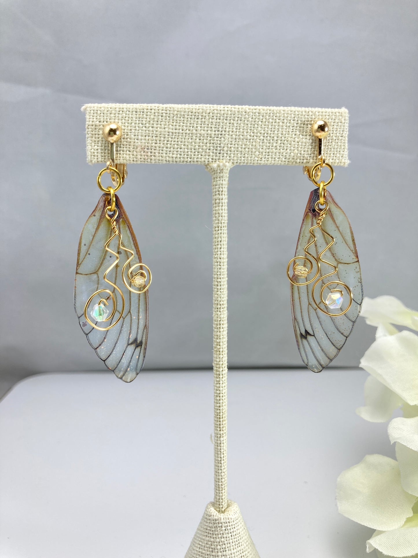 yellow butterfly wing clip on earrings dangling from an earring display with a yellow flower in the background