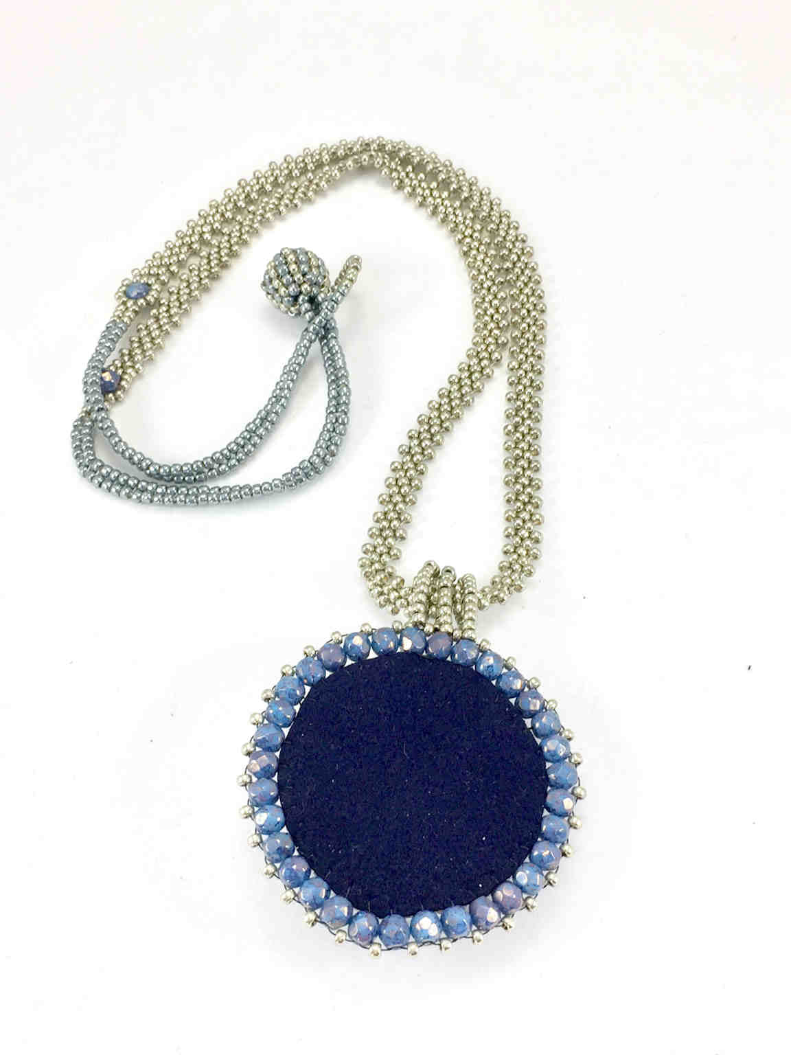 Back of A necklace with a blue faux suede surrounded by silver and blue beadwork on a long silver seed bead chain with blue crystals and ball and loop closure