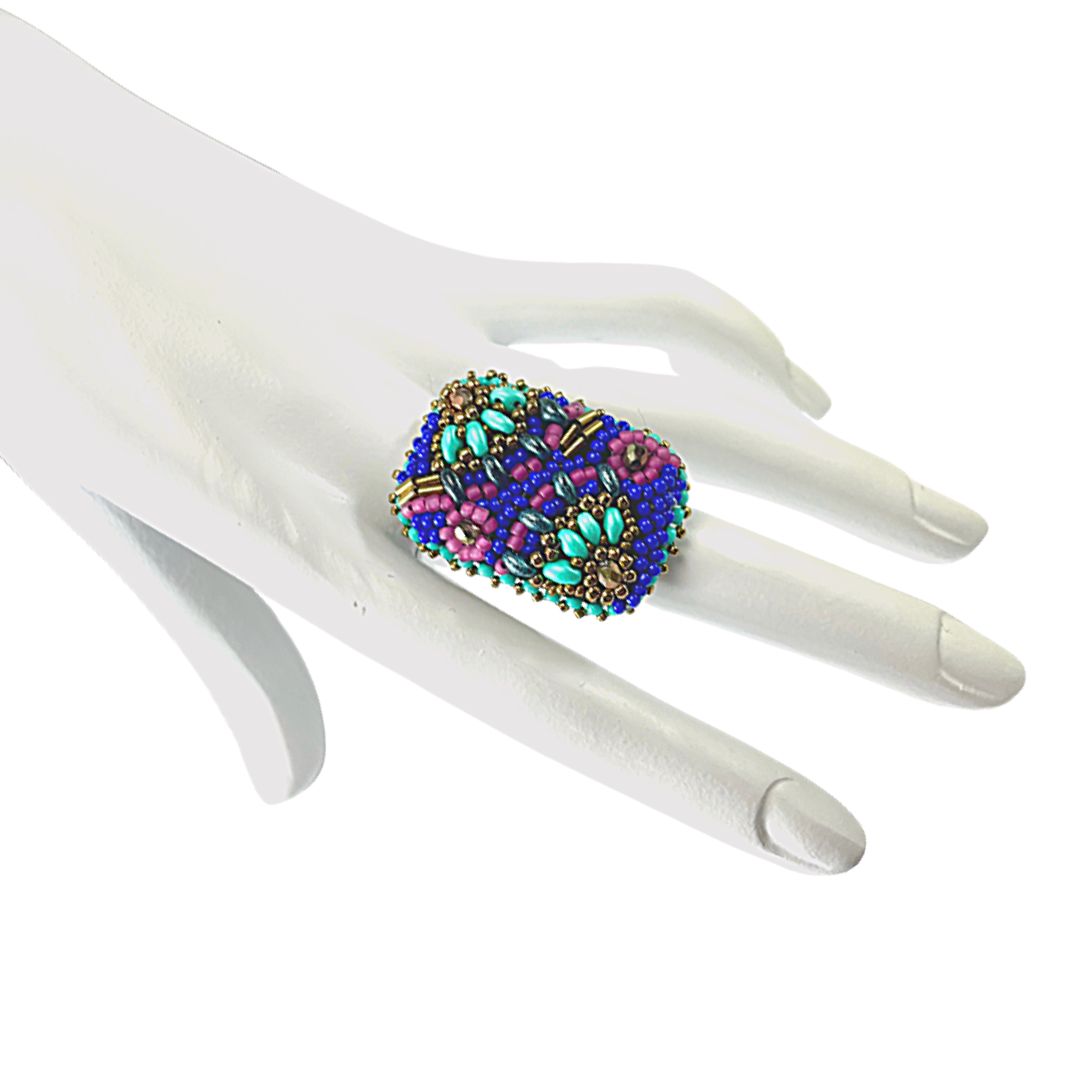 Hand beaded rectangle ring with pink and turquoise flower with bronze crystals and with gold and royal blue glass bead details. on hand model.