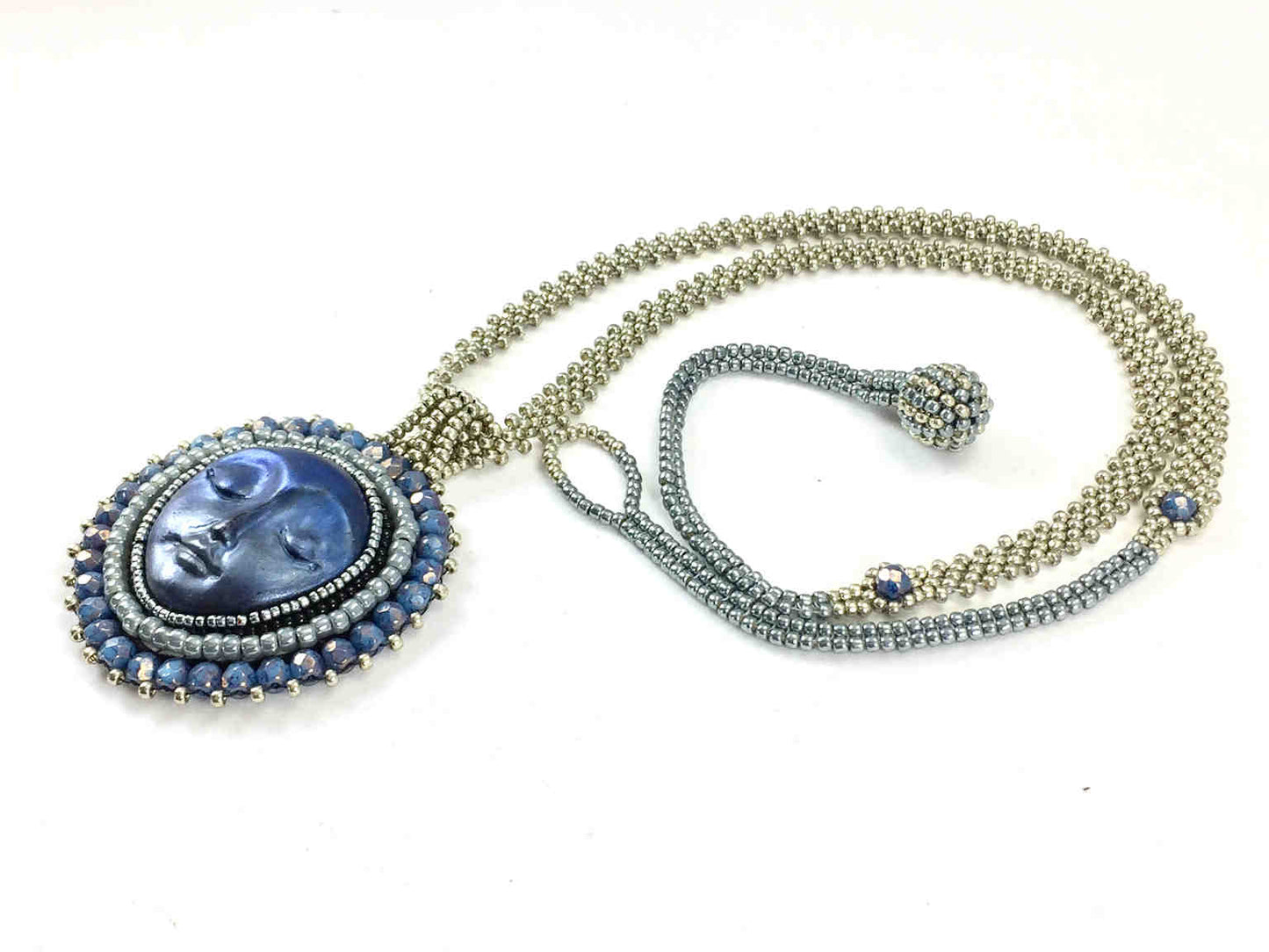 Side profile of A necklace with a blue moon face surrounded by silver and blue beadwork on a long silver seed bead chain with blue crystals and ball and loop closure