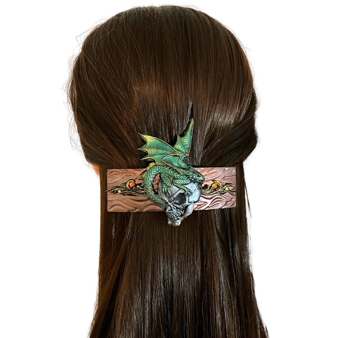 Polymer clay hair copper color hair barrette with Gray skull with green dragon sitting on top. Filigree detail in gold to sides of skull with colorful crystals. on model's hair..