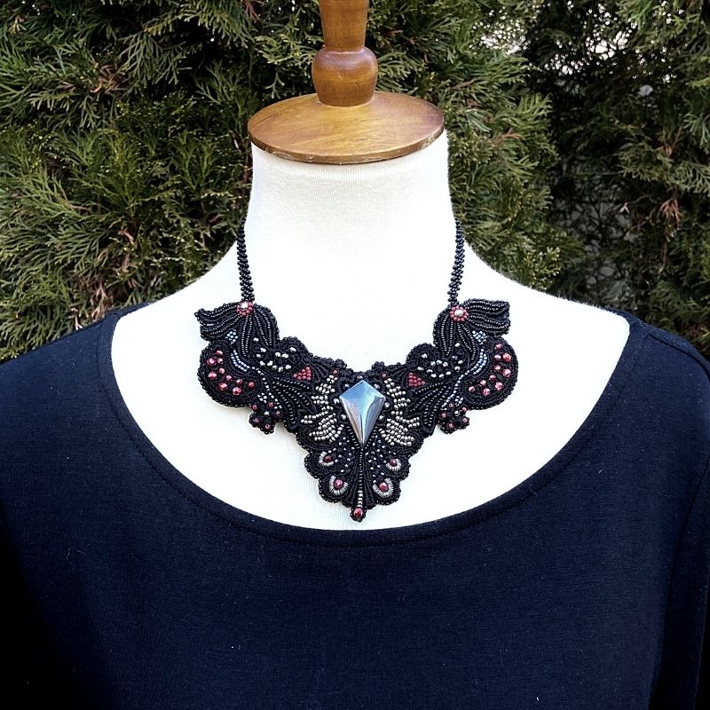 Large gothic beaded collar necklace with hematite beads display on a model  with a black dress outside with a fir tree in the background