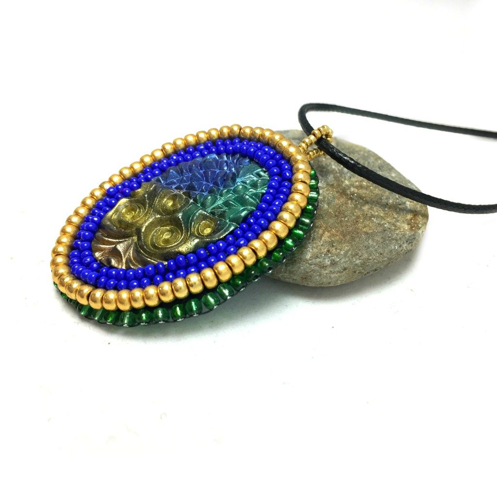 Side profile of blue green and gold zentangle pattern pendant with blue and gold beaded edge.