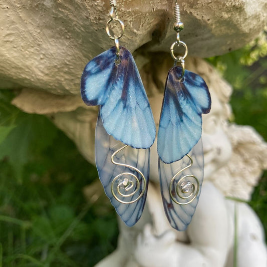 Blue butterfly double wing earrings with silver wired swirls with a silver crystal in center. On silver colored fishhook earrings photoraphed outside with a fairy garden ornament in the background.