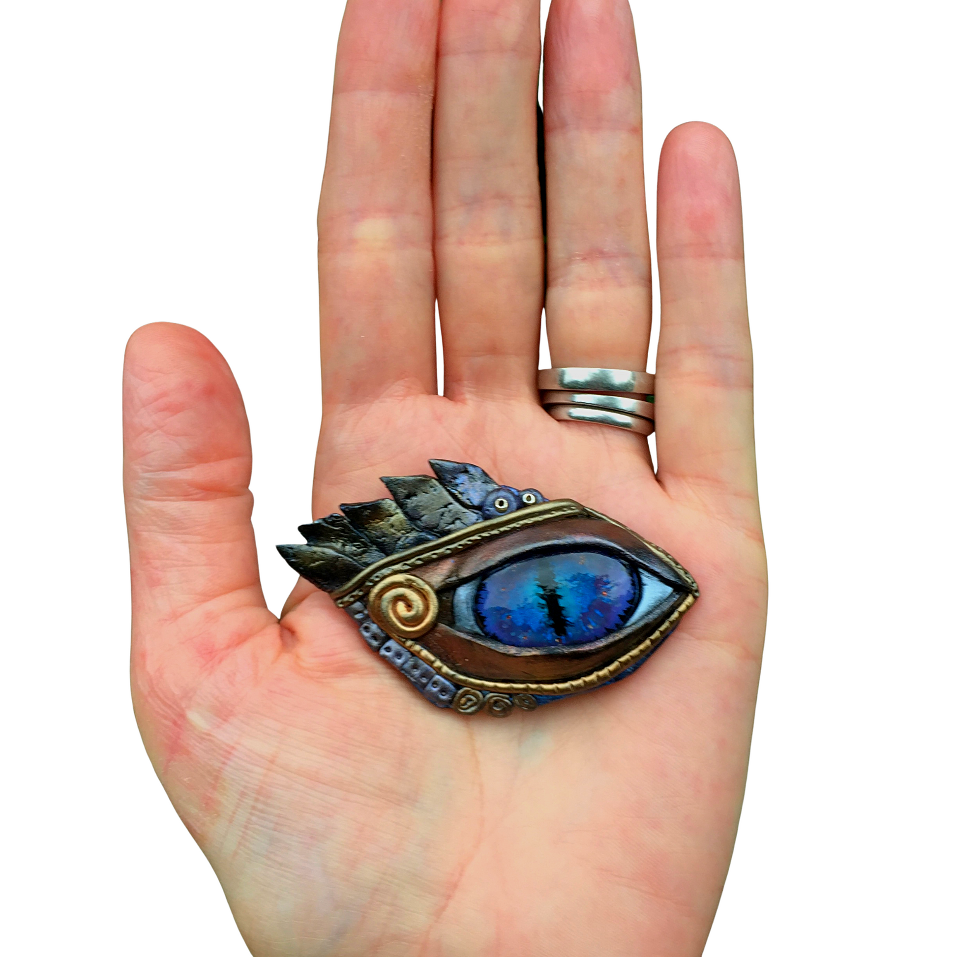 egyptian blue eye brooch with gold and bronze feather details and gold swirl at corner of the eye in a hand.