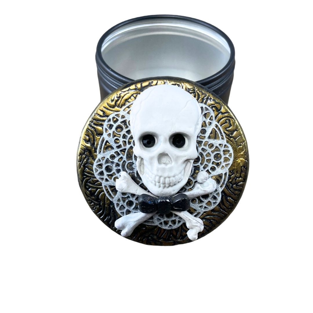 White skull and crossbones with black crystal eyes and dickie bow against white lace clay and gold textured lid of a storage jar.