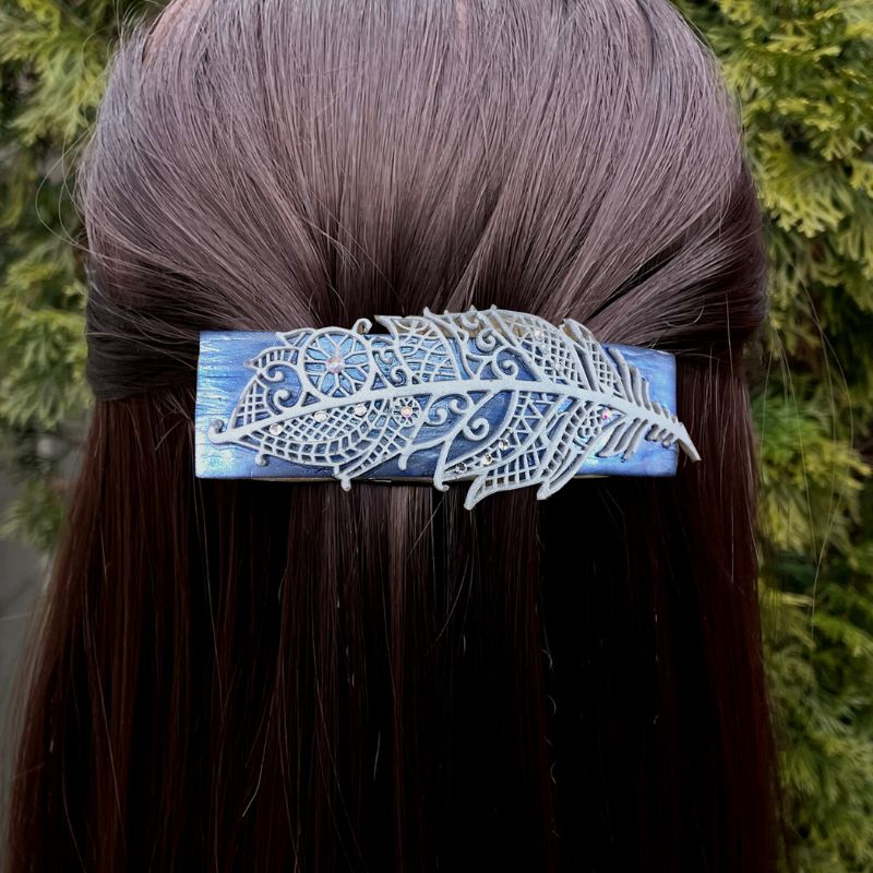 Silver blue polymer clay handmade hair barrette with silver clay mandala feather and crystals with rainbow luster dotted around the feather design. In model's hair.