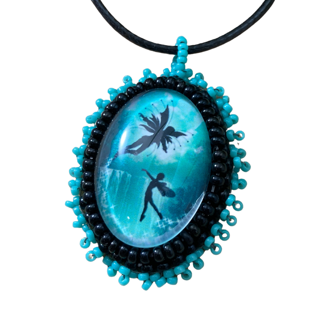 Teal green oval pendant with glass cabochon with flying fairies flying.  Surrounding beadwork in black and teal seed beads.