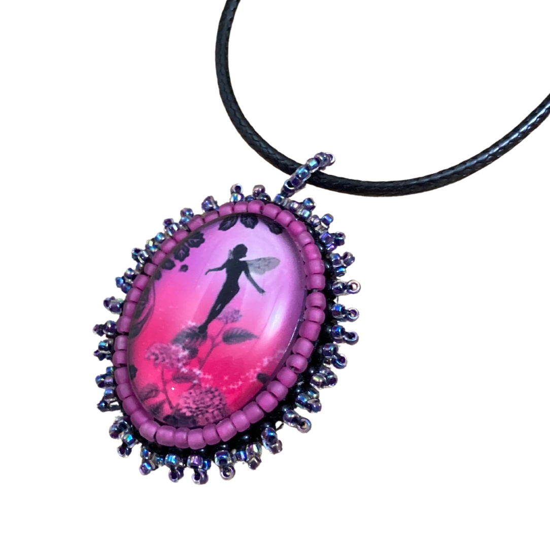Hot pink glass cabochon oval pendant with fairy silhouette flying among flowers.  Seed bead edging in black oil slick seed beads.