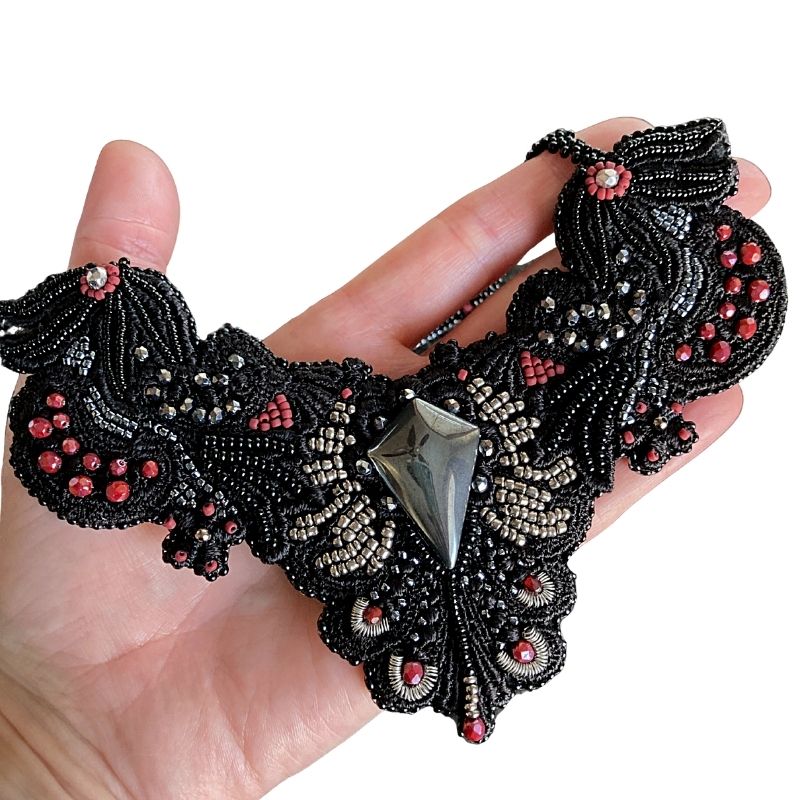 Gothic collar statement necklace with hematite cabochon and bead embroidery held in a hand for size reference