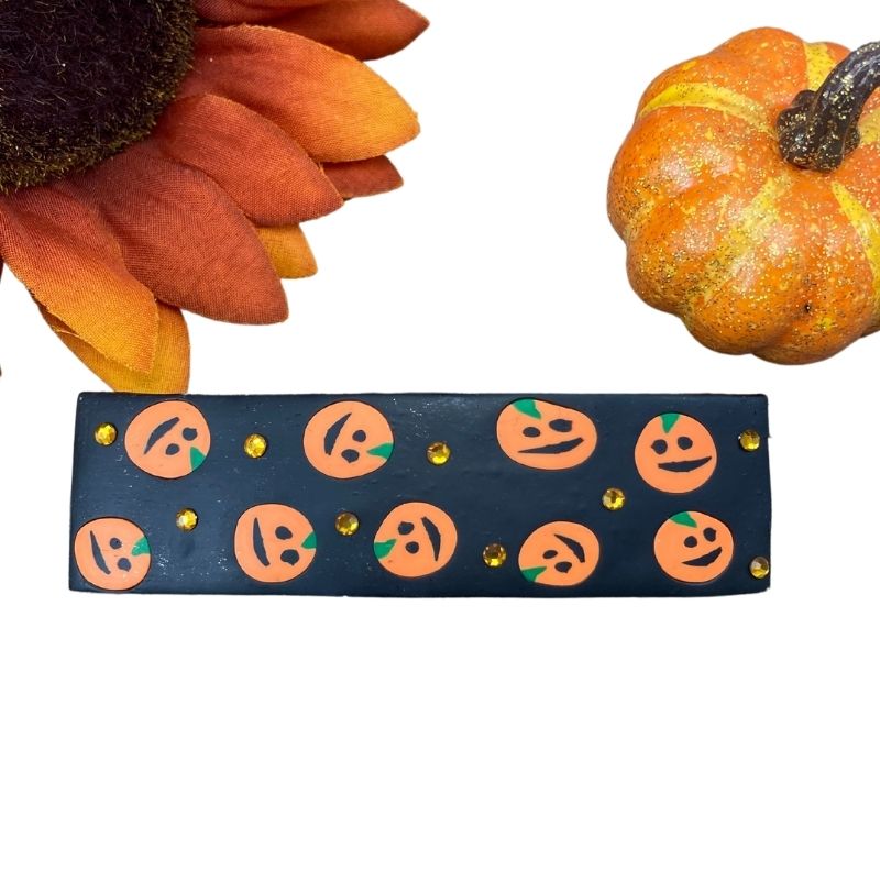 Halloween hair clip with mini orange pumpkins with faces and orange crystals. An orange pumpkin and sunflower are in the background.