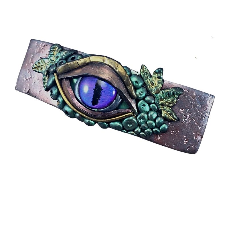 left view of a purple and gold mal de ojo aka evil eye in the form of a hair barrette