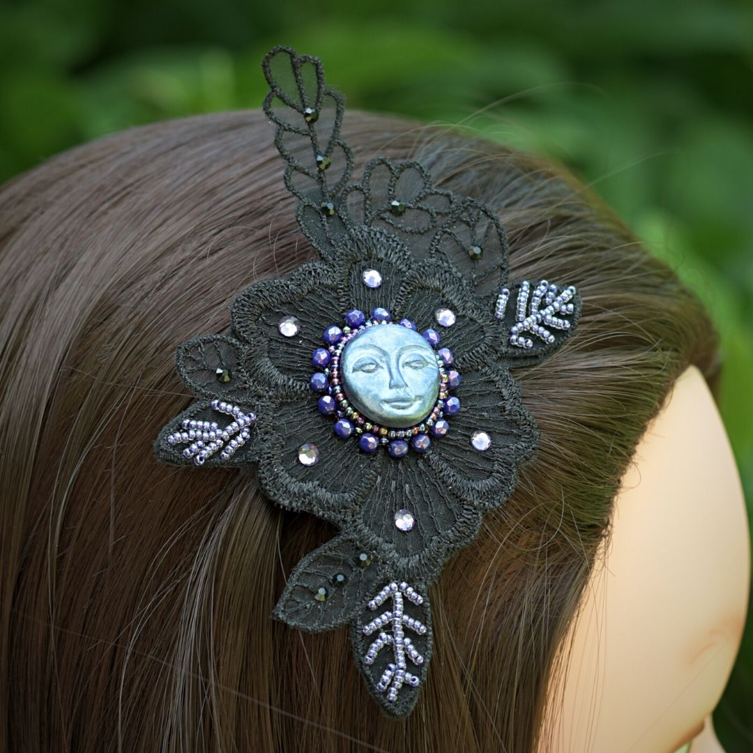 whimsigothic hair clip with blue moon and purple beading on black lace applique on a model in a garden.