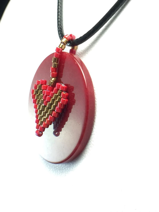 Round burgundy Jasper oendant with red and gold beaded heart charm on a black cord necklace.