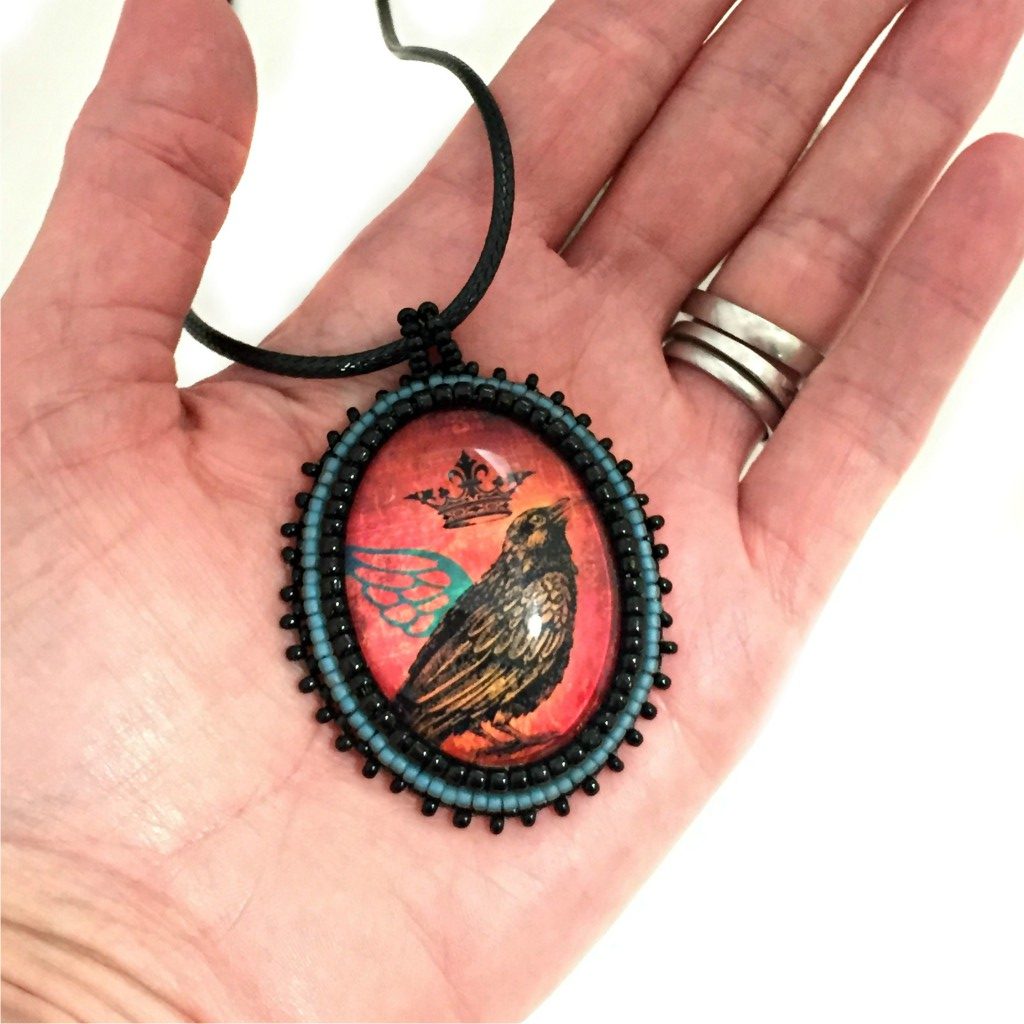 raven with teal wing pendant in hand