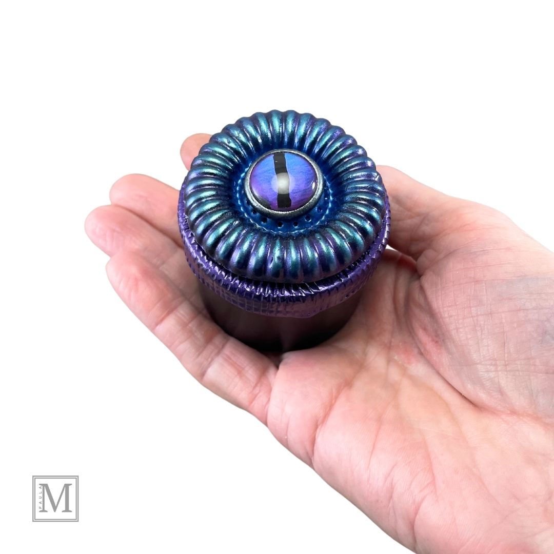 Purple and Blue polymer clay textured design lid with glass purple evil eye in a hand.