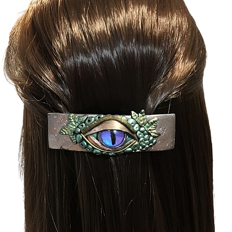 A purple and gold third eye hair clip with leaves and green forest leaf details