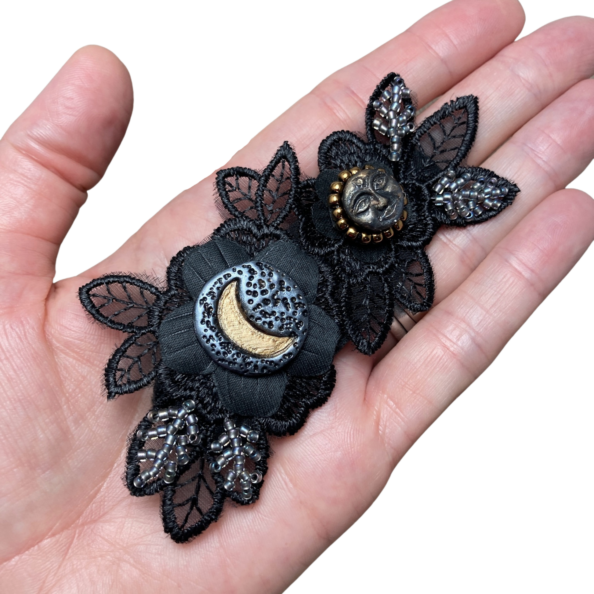 Black applique flower beaded with silver and gold beads with a crescent moon and a full face moon focal cabochons in a hand